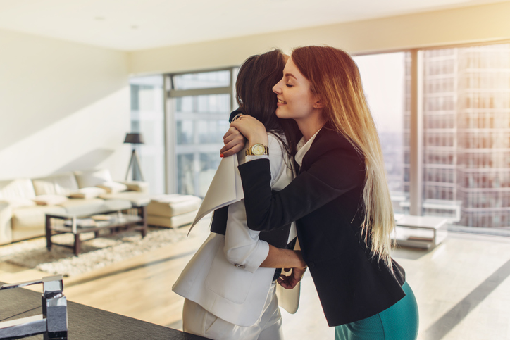 Happy customer hugging her real estate agent after successful deal. Young woman purchasing a loft apartment from realtor.