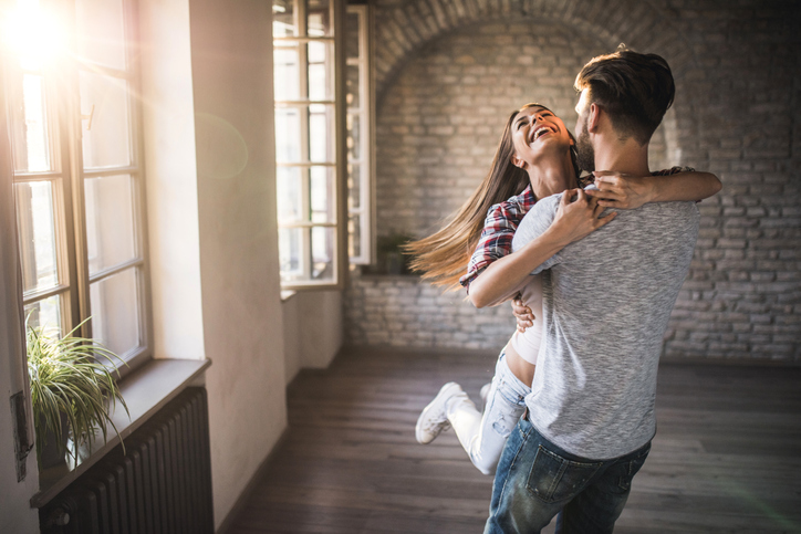 Young joyful couple having fun while spinning in their new home.